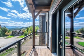 Un balcon en bois avec une porte vitrée, donnant sur un quartier résidentiel avec des maisons et un ciel dégagé.