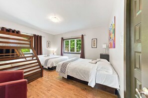 A hotel room with two beds, a wooden staircase, a red chair, and a window with a view of greenery. - Spa & Billard | BLANC 21- Stoneham Chalet (Stoneham-et-Tewkesbury)