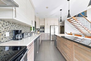 A modern kitchen with a central island, stainless steel appliances, and a tiled backsplash. - Spa & Billard | BLANC 21- Stoneham Chalet (Stoneham-et-Tewkesbury)