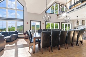 Un vaste espace de salle à manger avec un haut plafond et de grandes fenêtres, une cuisine moderne offrant une vue dégagée et un coin salon confortable avec vue.