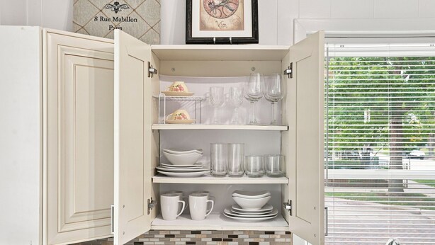 A kitchen with open cabinets displaying dishes, glasses, and a framed picture above. - Charming One Bed with Office near Chicago! (Forest Park)