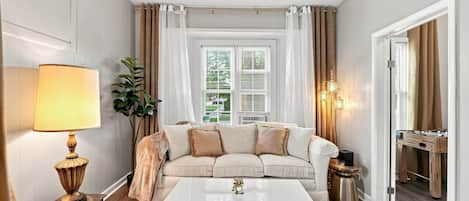 Una sala de estar con sofá, mesa de centro, lámpara y ventana con cortinas.