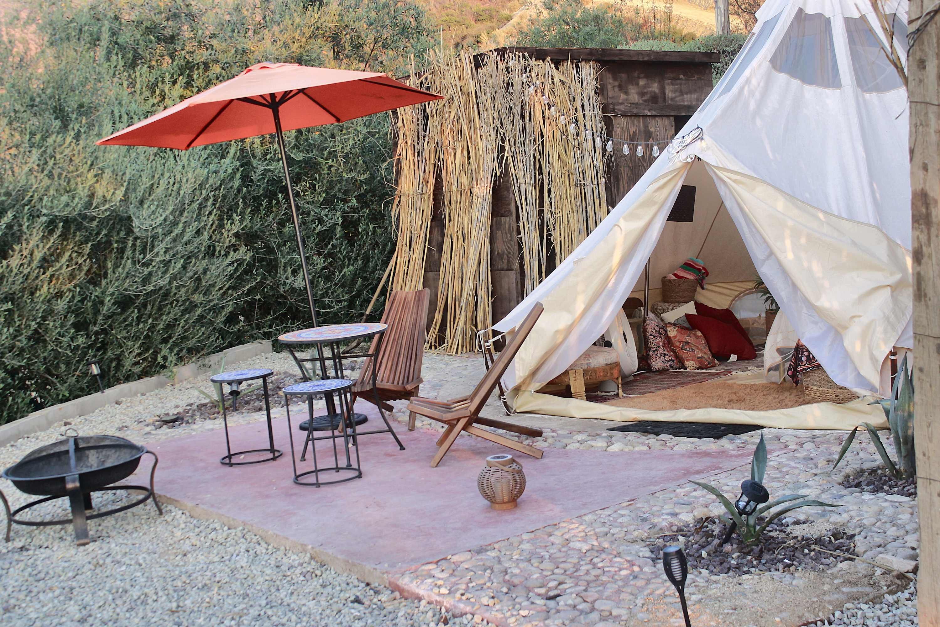 A tent with a white interior, a red umbrella, and a table with chairs in a garden setting.