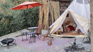 A tent with a white interior, a red umbrella, and a table with chairs in a garden setting.