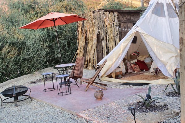 A tent with a white interior, a red umbrella, and a table with chairs in a garden setting.