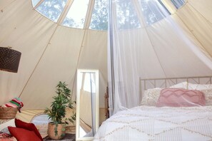 A tent interior with a bed, a hanging light fixture, and a potted plant.