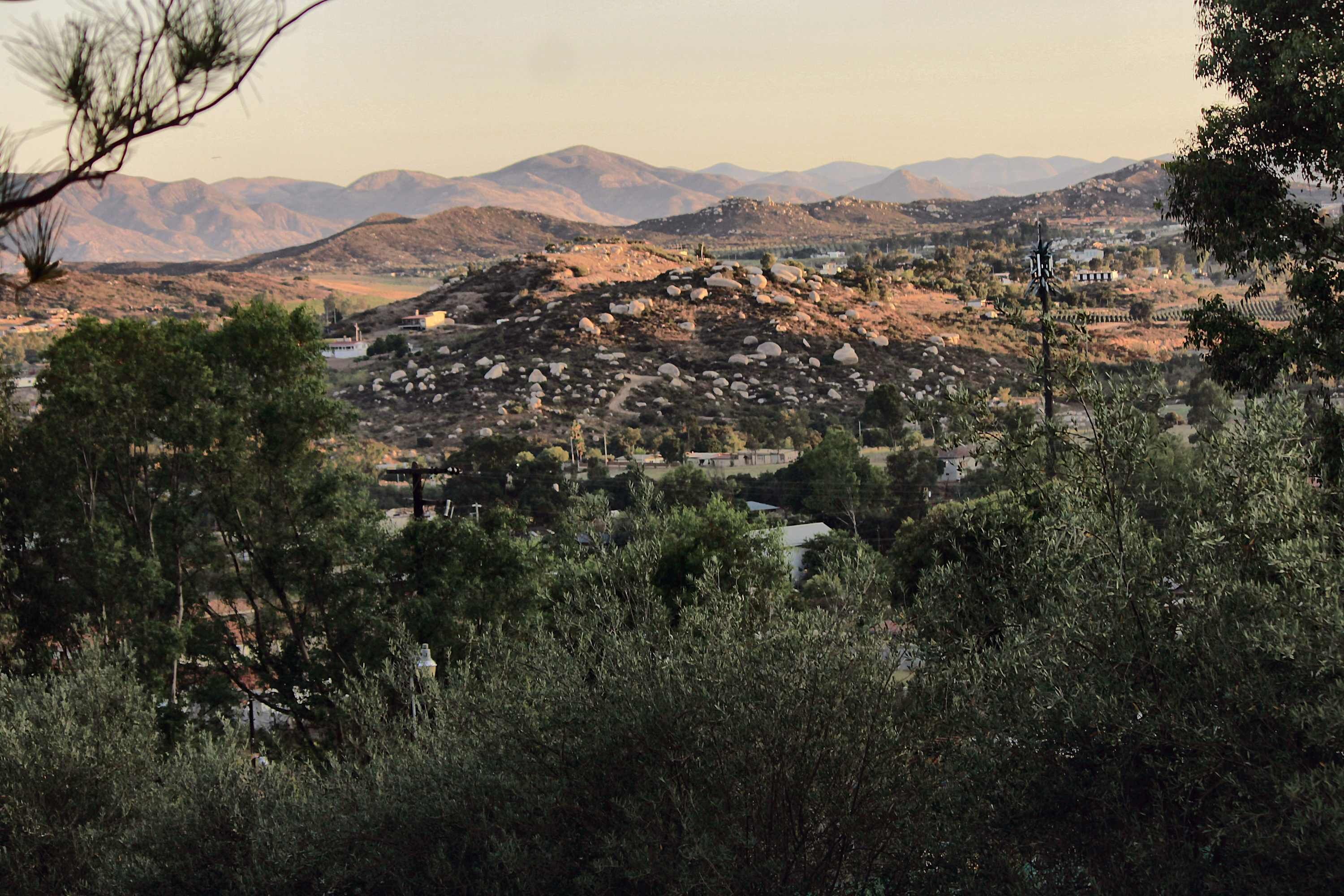 A mountainous landscape with scattered buildings, dense vegetation, and a clear sky.