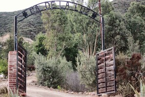 A metal archway with the inscription 'TAKE THE ROAD' leading to a dirt path surrounded by vegetation.