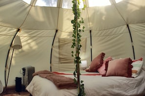 A tent with a bed, pillows, a blanket, a lamp, and a radiator.