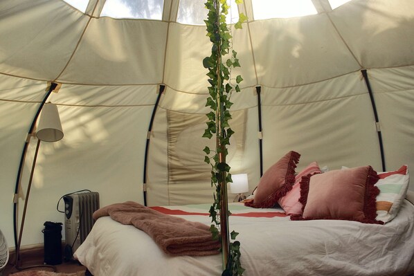 A tent with a bed, pillows, a blanket, a lamp, and a radiator.