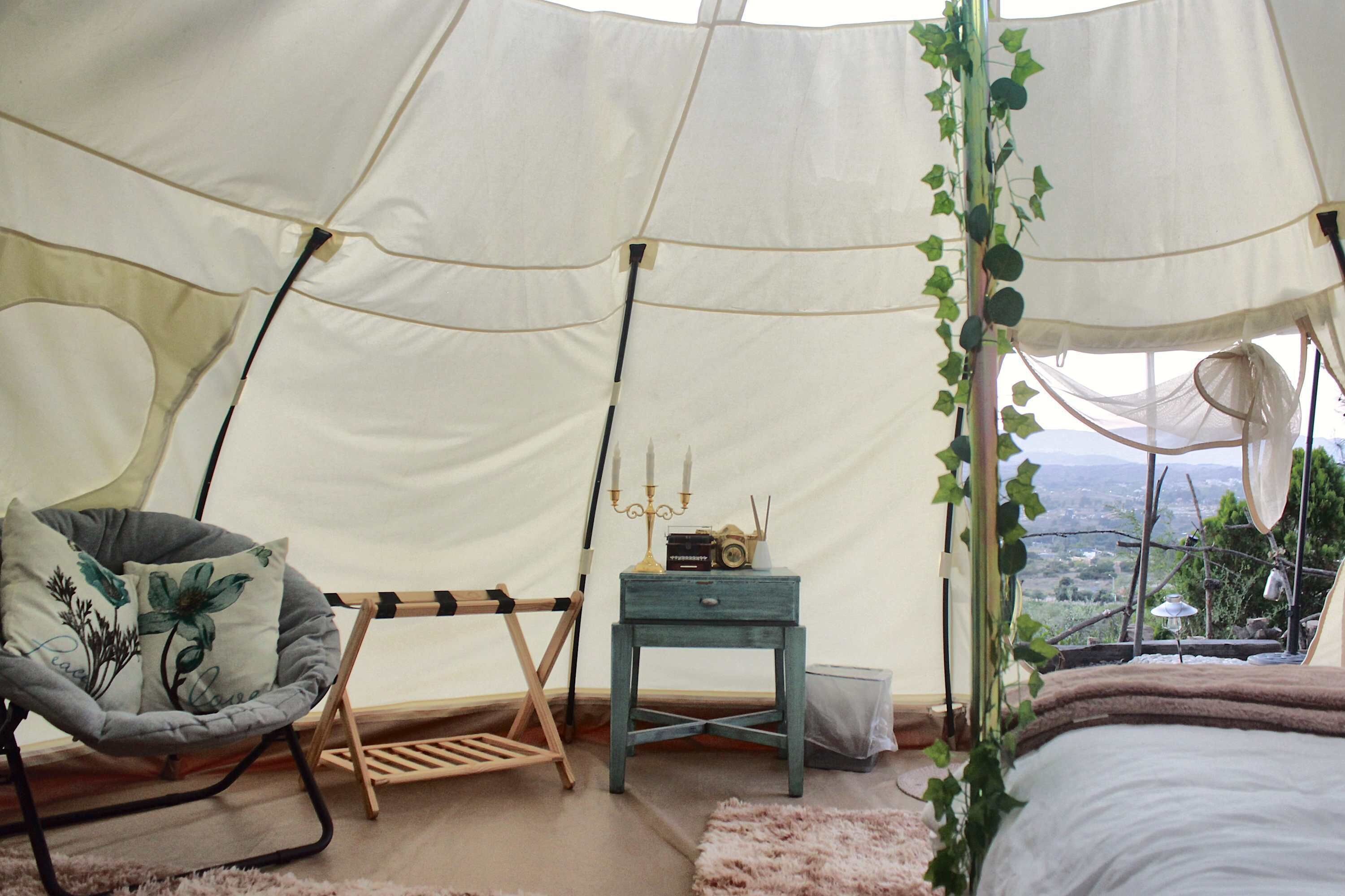 A cozy tent interior with a cushioned chair, a small table with a decorative item, and a view of the outdoors.