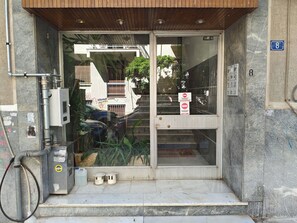 A building entrance with a glass door, a metal utility box, and a number sign. - Athenian Apt with Balcony Pagkrati by GHH (Athina)