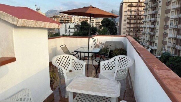 A balcony with white plastic chairs and a table, an umbrella, and a view of surrounding buildings. - Casa Rosina, nestled in a typical neighborhood atmosphere with everything just a stone's throw away. (Palermo)