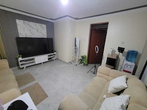 A living room with a sofa set, a flat-screen TV, a water dispenser, and a door. - Tranquil 1-bedroom apartment in wonderful Nairobi neighborhood (Nairobi)