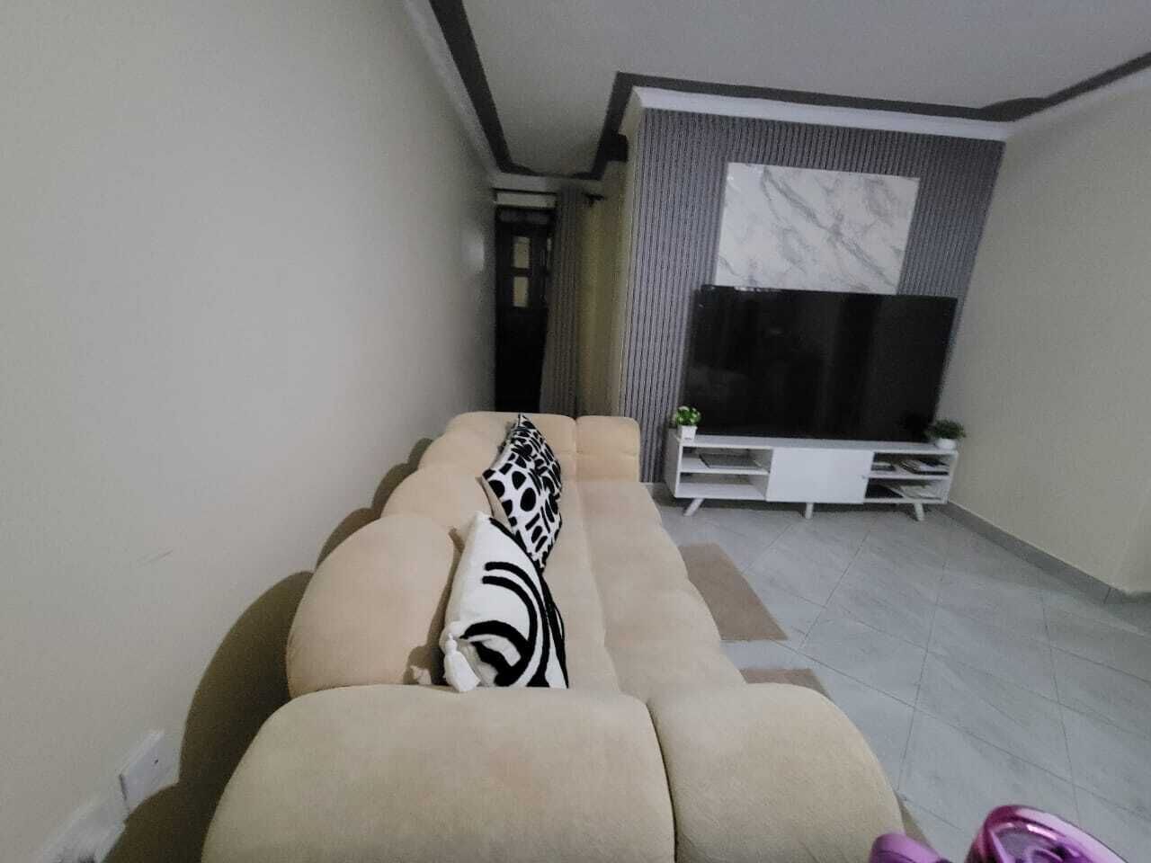 Un salon comprenant un canapé, un téléviseur à écran plat et un meuble de rangement blanc.