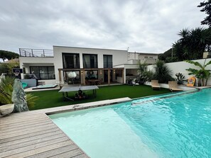 Une maison moderne dotée d’une piscine, d’un patio et d’un panier de basketball.