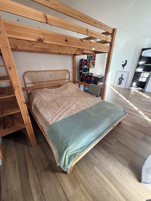 Un lit superposé avec une structure en bois et une échelle, un lit recouvert d’une housse à motifs et un mur orné de posters encadrés.
