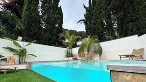 Ein Swimmingpool mit klarem, blauem Wasser, umgeben von einer weißen Mauer und einer Rasenfläche mit einer Liege.