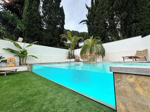 A swimming pool with a clear blue water, surrounded by a white wall, and a grassy area with a lounge chair. - Villa near the beaches and all amenities (La Grande-Motte)