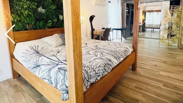 Ein Zimmer mit einem Bett unter einem Holzbalkon, einem Essbereich und Blick auf ein weiteres Zimmer.