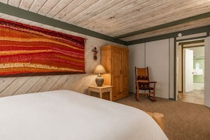 A bedroom with a large bed, a wooden wardrobe, a chair, a lamp, and a vibrant tapestry on the wall. - Short Walk to Canyon 683 (Mammoth Lakes)