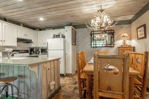 A kitchen with white cabinets, a wooden island, a chandelier, and a dining area with wooden chairs. - Short Walk to Canyon 683 (Mammoth Lakes)