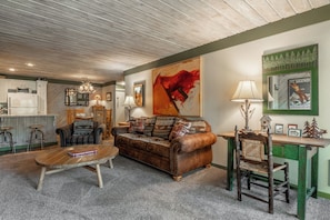 A cozy living room with a leather sofa, a wooden coffee table, and a dining area with a green wall and a framed poster. - Short Walk to Canyon 683 (Mammoth Lakes)