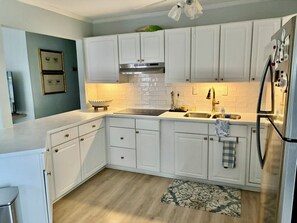 A kitchen with white cabinets, a stainless steel sink, and a refrigerator. - 4-bedroom house in soothing Penhook with cool AC breeze (Penhook)