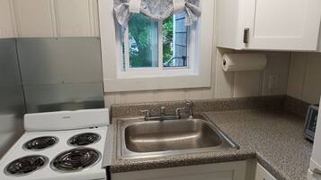 Una cocina con un horno blanco, un lavamanos de acero inoxidable y una ventana con un cortinero estampado.