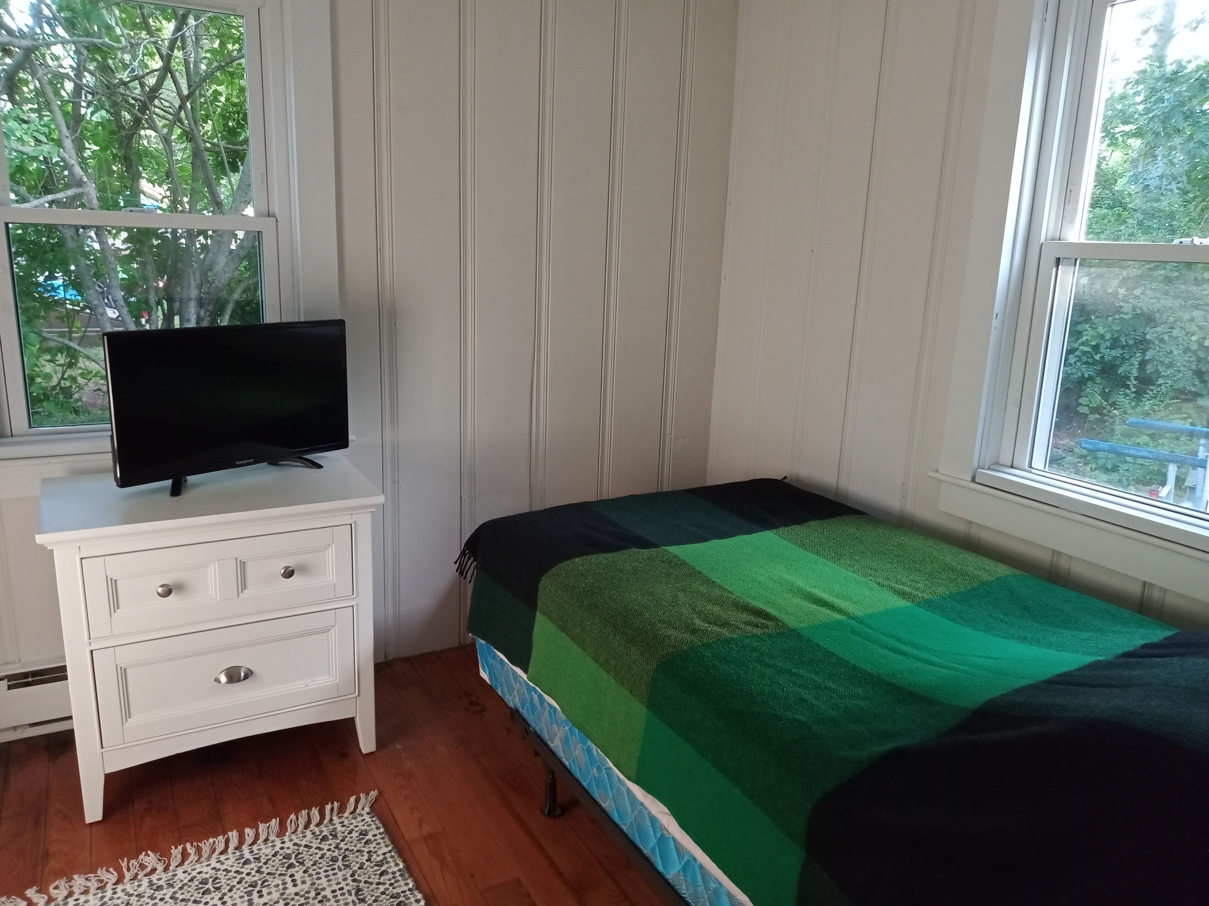 A bedroom with a bed, a TV on a dresser, a window, and a view of trees.