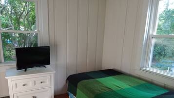 A bedroom with a bed, a TV on a dresser, a window, and a view of trees.
