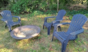 Trois chaises Adirondack et un foyer sont installés dans un espace extérieur verdoyant, avec un feuillage dense en arrière-plan.