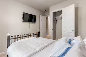 Un dormitorio con una cama, un televisor montado en la pared y un armario con la puerta abierta.