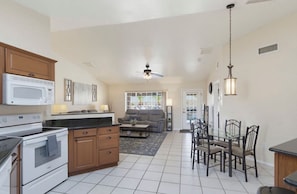 A kitchen with a microwave, stove, and cabinets, a dining area with chairs and a table, and a living room with a sofa and a TV. - Rango Desert Retreat with Private Pool (Lake Havasu City)