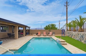A swimming pool with lounge chairs, a covered patio area, and a stone wall with palm trees. - Rango Desert Retreat with Private Pool (Lake Havasu City)