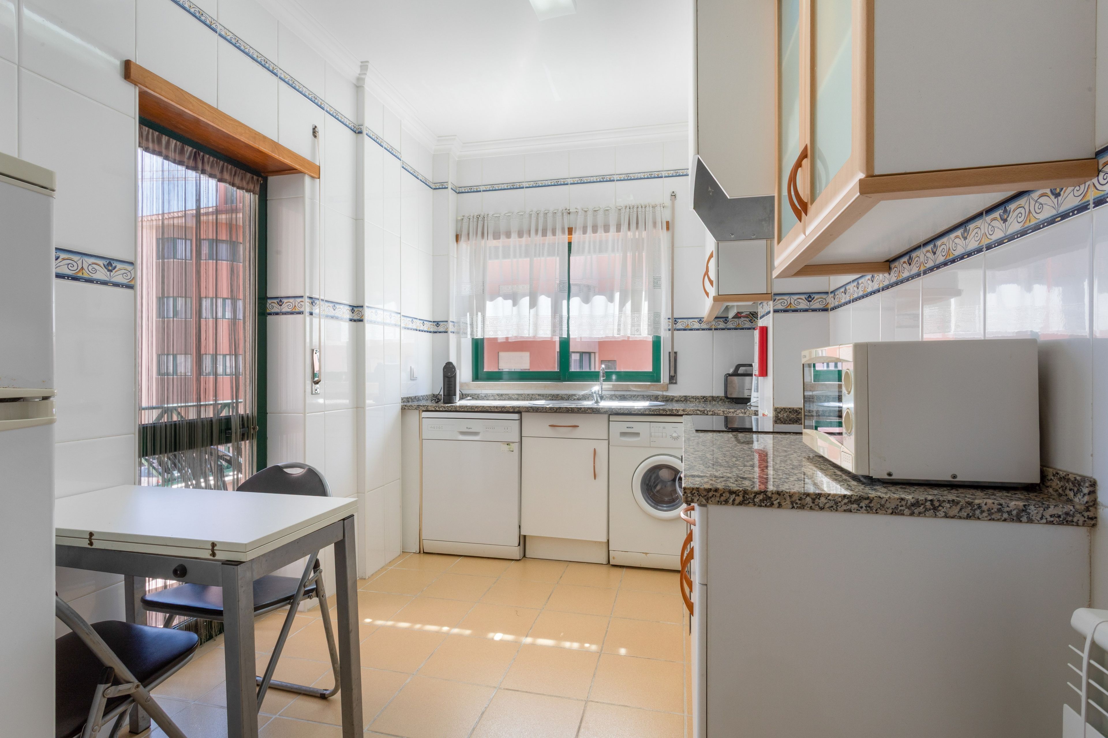 Cozinha compacta com máquina de lavar, pia e área de refeições com mesa e cadeiras.