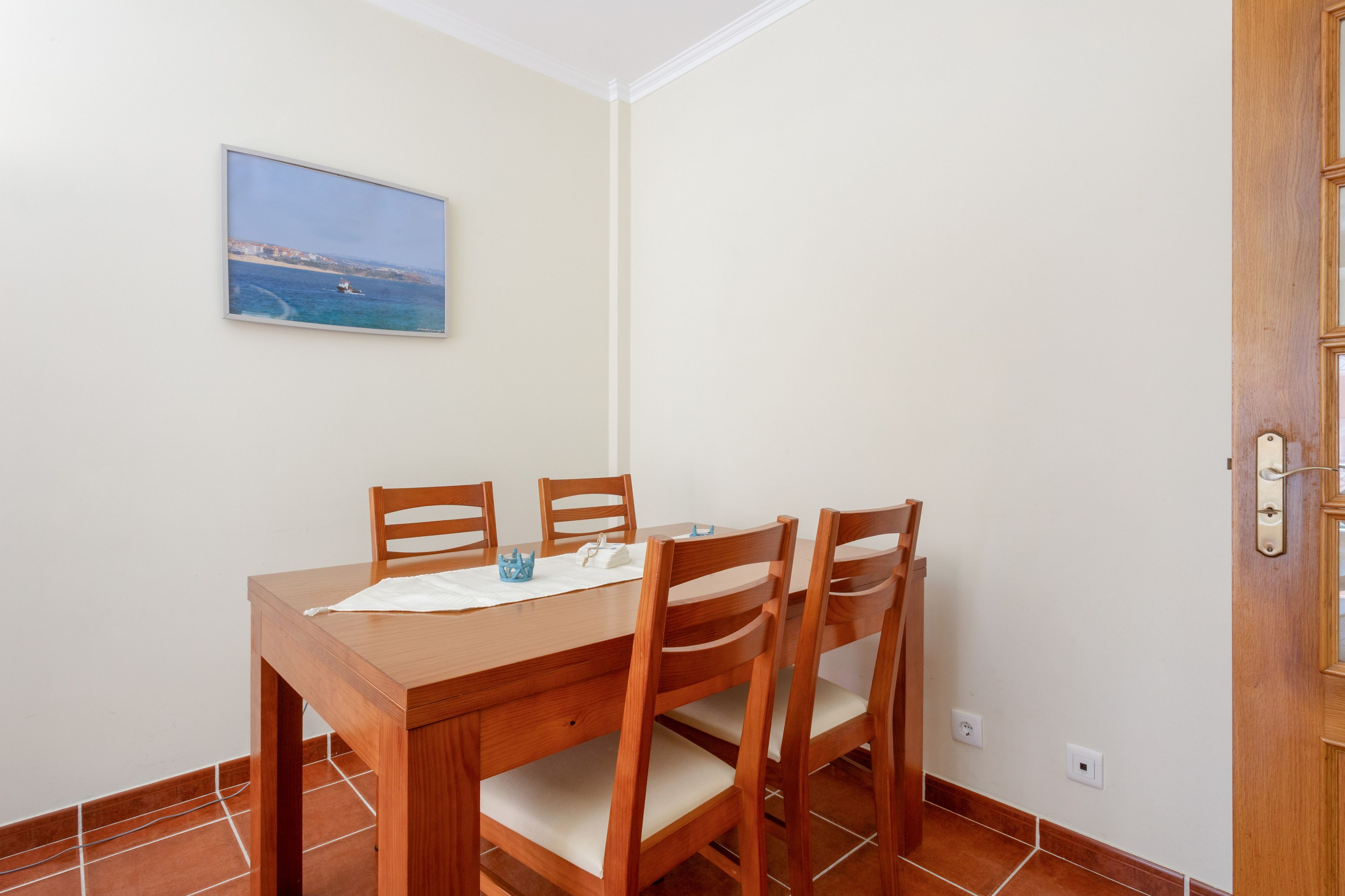 A dining area with a wooden table and four chairs, a small decorative item, and a framed picture on the wall.