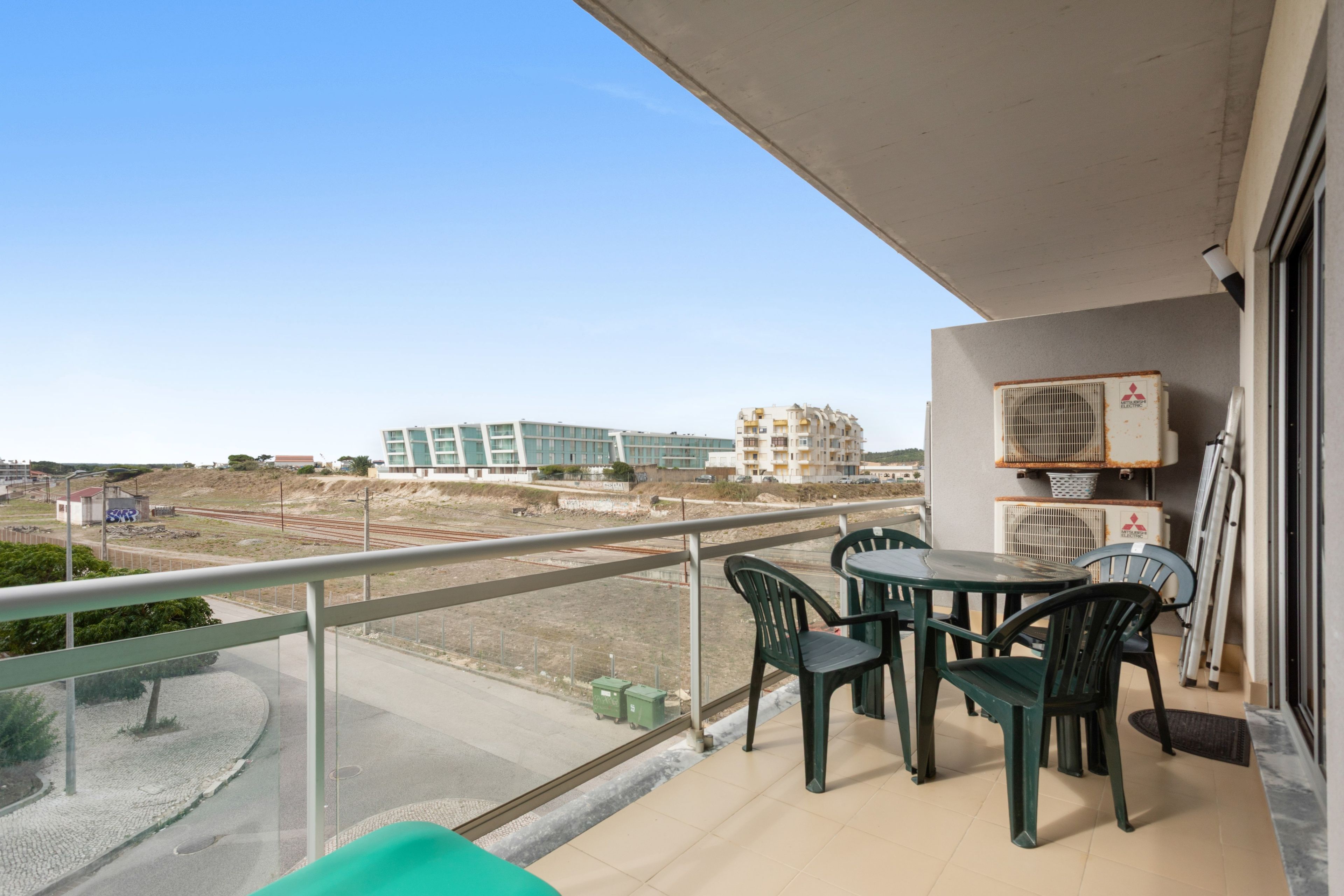 Un balcón con mesa y sillas, con vistas a una obra en construcción y edificios.