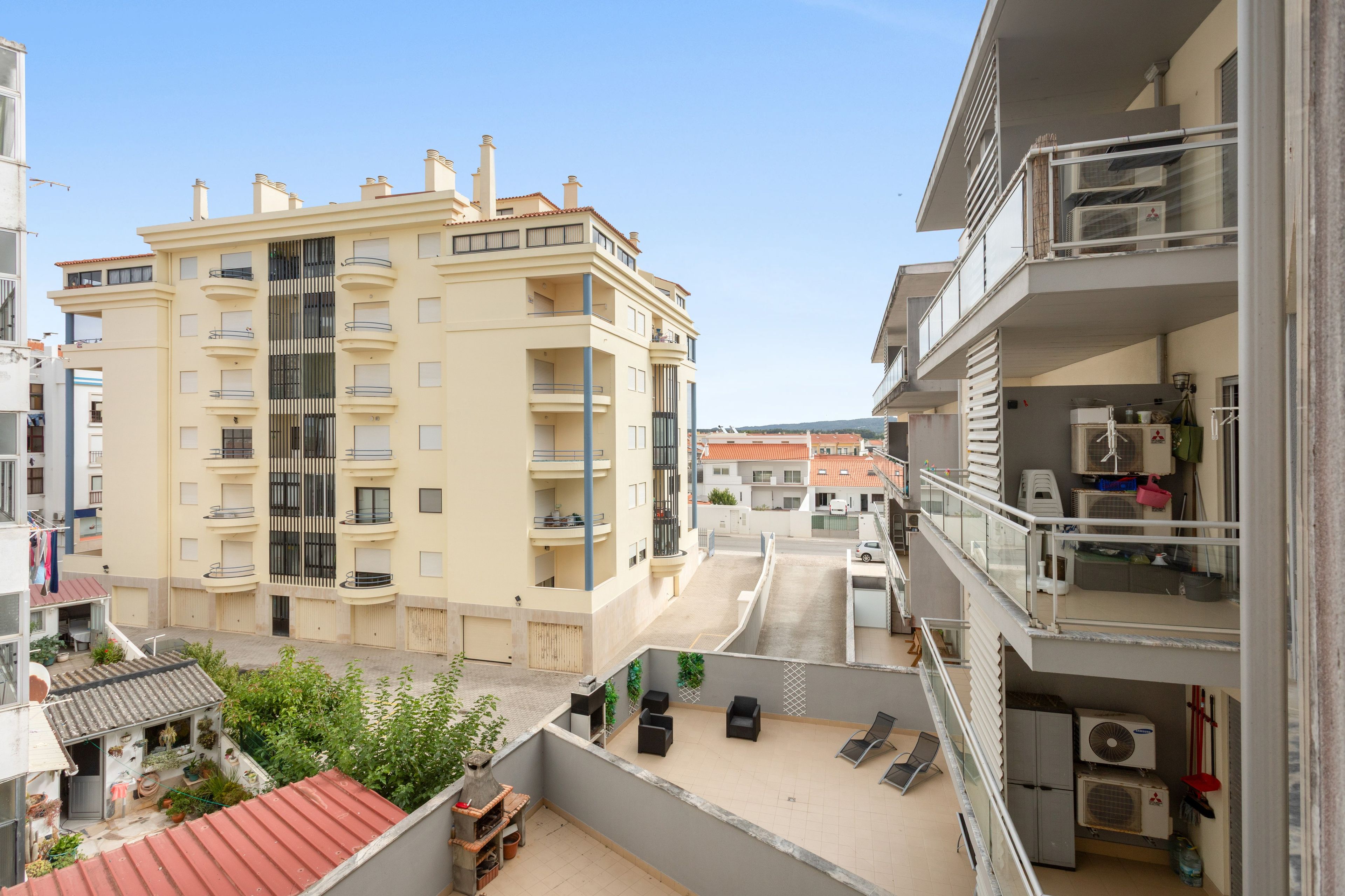 Un immeuble résidentiel à plusieurs étages, doté de balcons, d’un espace extérieur couvert aménagé en coin salon et offrant une vue sur la rue.