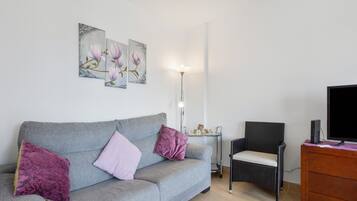 A living room with a grey sofa, a black chair, a TV, and a floor lamp.