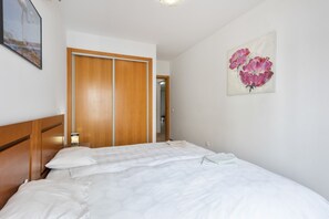 Habitación de hotel con cama, armario de madera, un cuadro de flores y mesita de noche con lámpara.