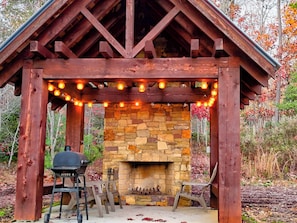 A stone fireplace with a wooden mantel, surrounded by a wooden pergola with string lights. - Cozy Cottage in the Foothills of Blue Ridge Mtns. (Clarkesville)