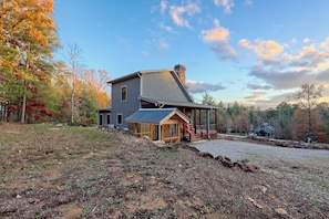 A two-story house with a stone chimney, a wooden porch, and a gravel driveway. - Cozy Cottage in the Foothills of Blue Ridge Mtns. (Clarkesville)
