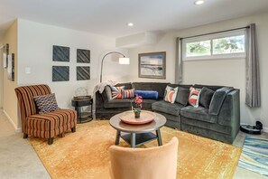 A living room with a striped armchair, a sofa, a round coffee table with a flower vase, and a large window with curtains. - Silver Spring Retreat Near DC | Pet Friendly Yard (Silver Spring)