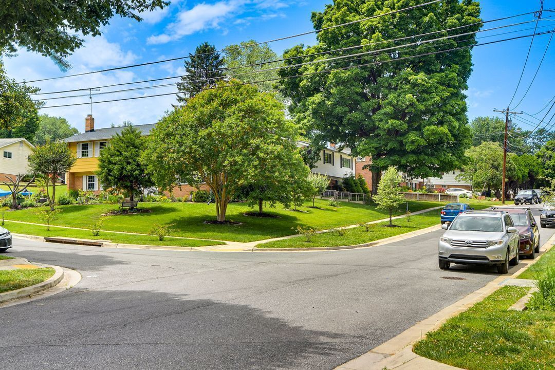 A residential street with houses, a car, and trees.