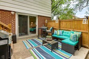 A backyard patio with a sliding glass door, a barbecue grill, a wicker sofa with cushions, and a striped rug. - Silver Spring Retreat Near DC | Pet Friendly Yard (Silver Spring)