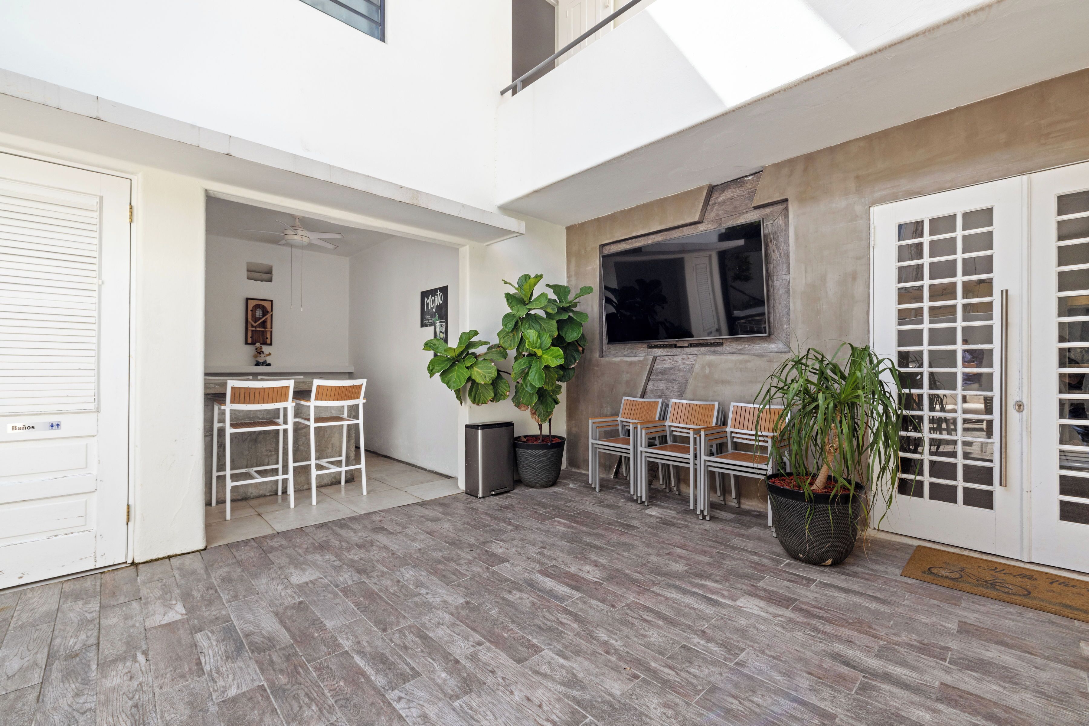 A spacious patio area with a ceiling fan, a TV mounted on a wall, and a seating area with chairs and tables.