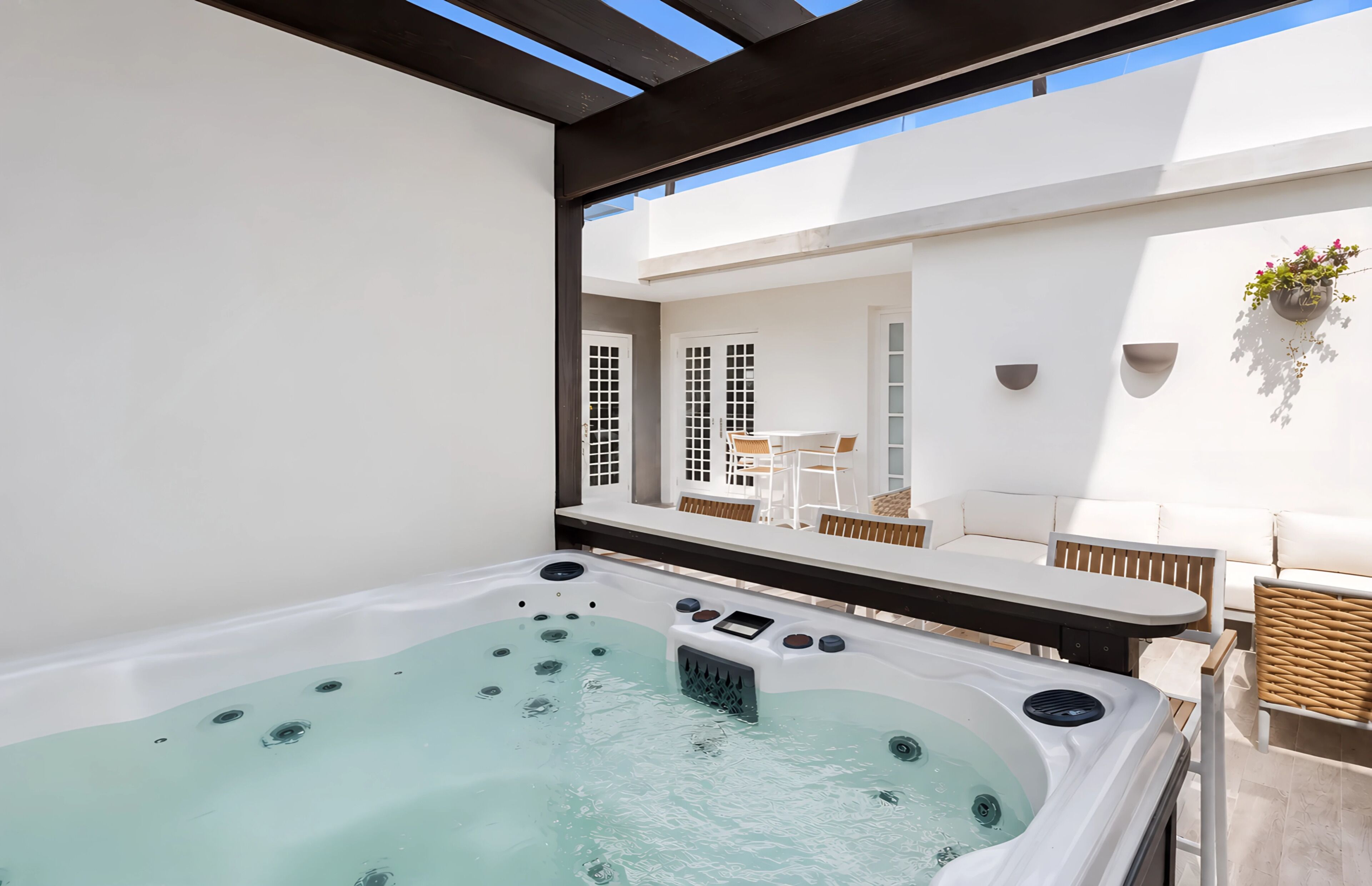 A hot tub with a control panel, a white outdoor seating area with a table and chairs, and a hanging plant.
