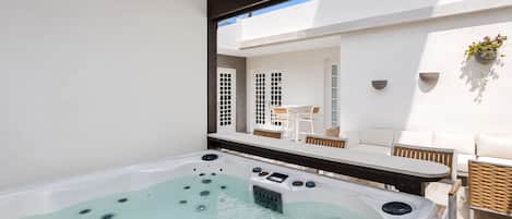 Un bain à remous doté d’un panneau de commande, un espace extérieur aménagé avec des meubles blancs, une table et des chaises, ainsi qu’une plante suspendue.