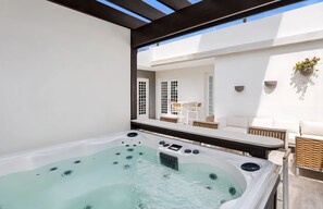 Ein Whirlpool mit Bedienfeld, ein weißer Außenbereich mit Tisch und Stühlen sowie eine hängende Pflanze.